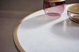 Nahaufnahme eines Couchtischs mit weißer Marmoroptik und goldener Umrandung, darauf stehen zwei dekorative Glasgefäße. Perspektive von oben.