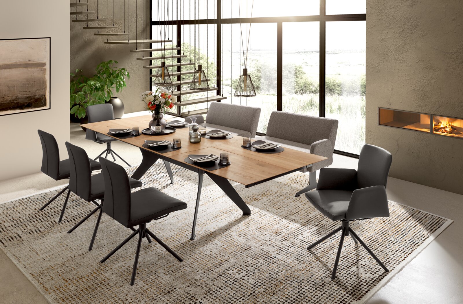 Modernes Esszimmer mit großem rechteckigen Esstisch aus Holz und schwarzen Metallbeinen, umgeben von grauen und schwarzen Polsterstühlen, aus schräger Frontansicht.
