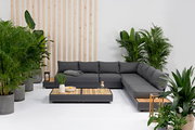 Moderne Gartenmöbel-Lounge mit grauem Ecksofa und Holztischen, umgeben von grünen Pflanzen, aus der Vorderansicht.