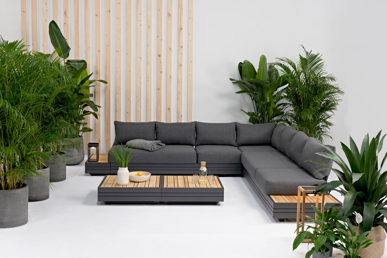 Zebra Loungesessel CUBO Moderne Gartenmöbel-Lounge mit grauem Ecksofa und Holztischen, umgeben von grünen Pflanzen, aus der Vorderansicht.