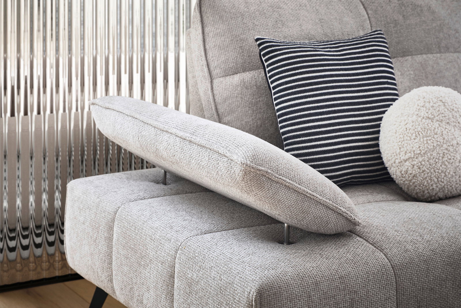 Nahaufnahme einer grauen Longchairkombination mit verstellbarer Armlehne, gestreiftem Kissen und rundem, flauschigem Kissen, seitliche Perspektive.