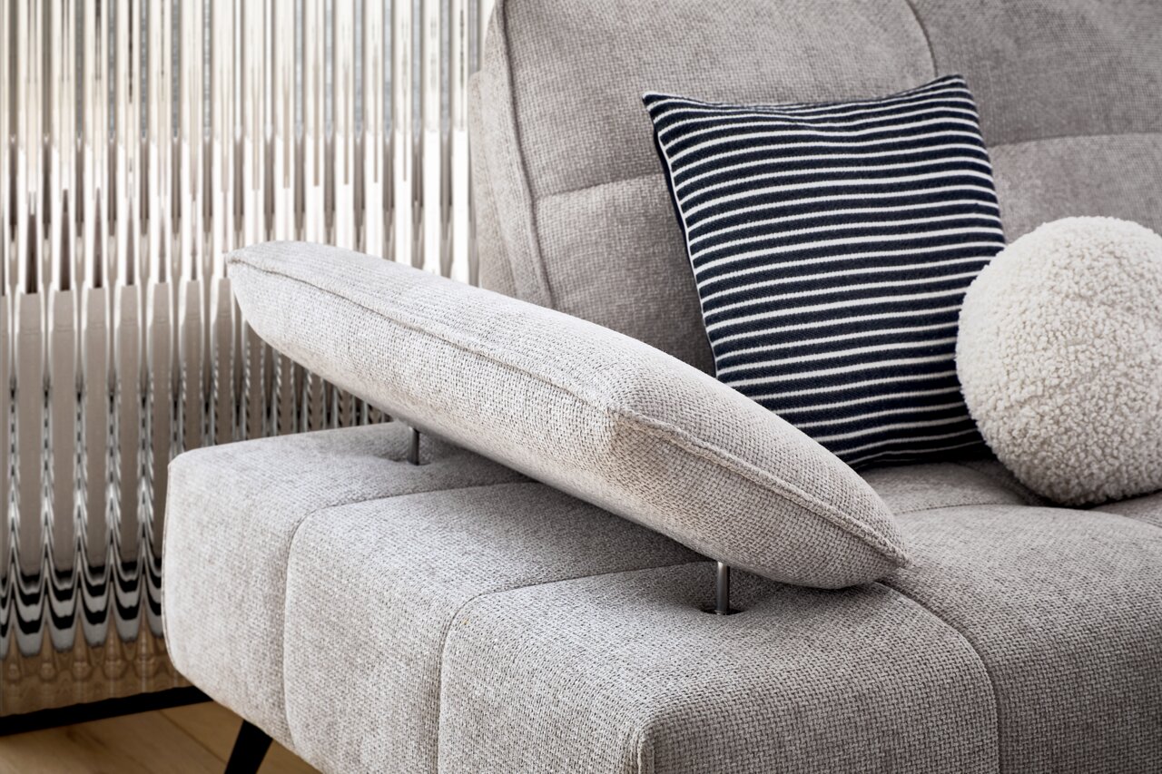 Nahaufnahme einer grauen Longchairkombination mit verstellbarer Armlehne, gestreiftem Kissen und rundem, flauschigem Kissen, seitliche Perspektive.