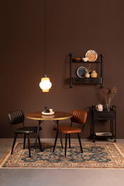 Ein stilvoll eingerichteter Raum mit einem runden Holztisch, zwei Stühlen und einem dekorativen Teppich in einem warmen, gemütlichen Ambiente. Der Teppich ist im Vordergrund zu sehen.