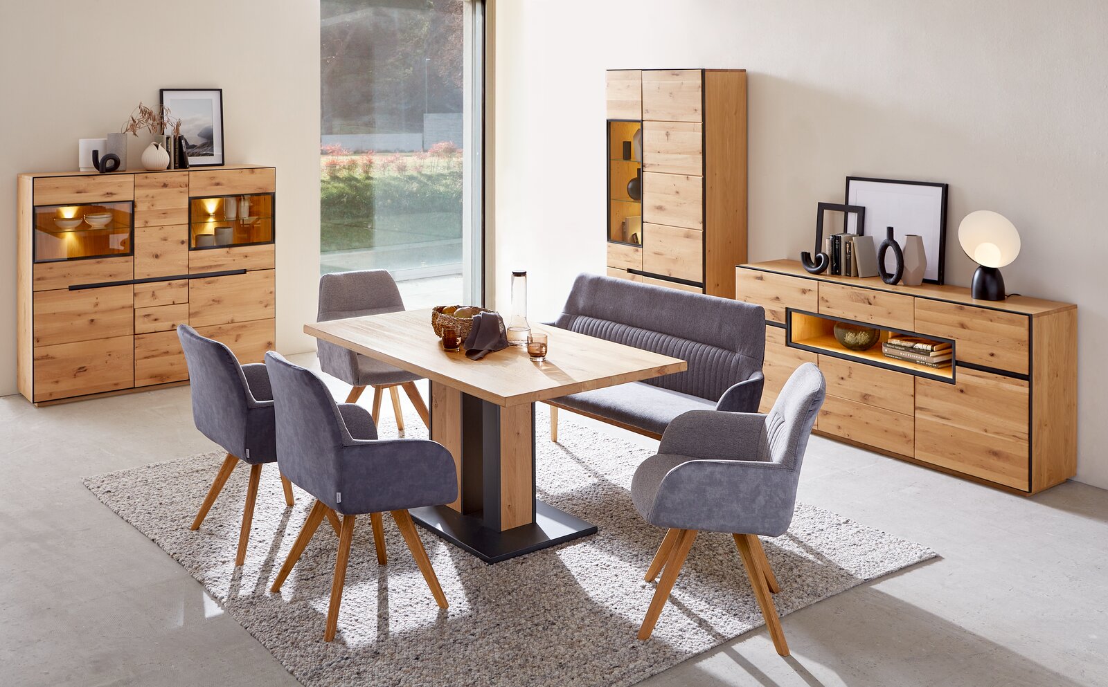 Moderner Esstisch aus Holz mit Metallfuß, umgeben von grauen Stühlen und einer Bank, in einem stilvoll eingerichteten Esszimmer mit Holzmöbeln. Perspektive: seitlich.