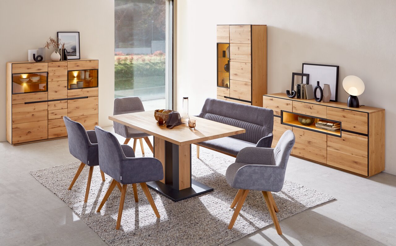 Moderner Esstisch aus Holz mit Metallfuß, umgeben von grauen Stühlen und einer Bank, in einem stilvoll eingerichteten Esszimmer mit Holzmöbeln. Perspektive: seitlich.