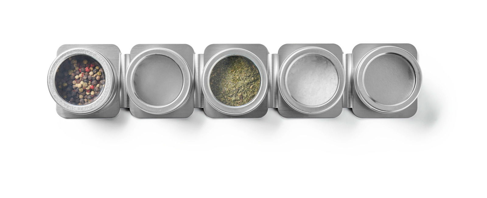 Vogelperspektive auf ein Gewürzdosenset aus Metall mit fünf runden Behältern, teilweise gefüllt mit Pfefferkörnern, Kräutern und Salz.