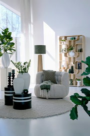 Modernes Standregal aus Holz mit geschwungenen Fächern, dekoriert mit Pflanzen und Vasen, in einem hellen Wohnzimmer mit großen Fenstern, seitliche Perspektive.