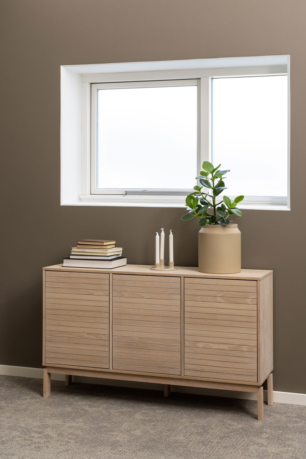 Modernes Sideboard aus hellem Holz mit drei Türen, dekoriert mit Büchern, Kerzen und einer Pflanze, seitliche Perspektive.