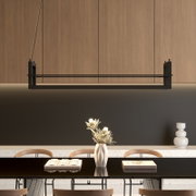 Moderne, rechteckige Pendelleuchte in Schwarz über einem Esstisch, frontale Perspektive; im Hintergrund Holzschränke und dunkle Wand, auf dem Tisch Vase und Bücher.