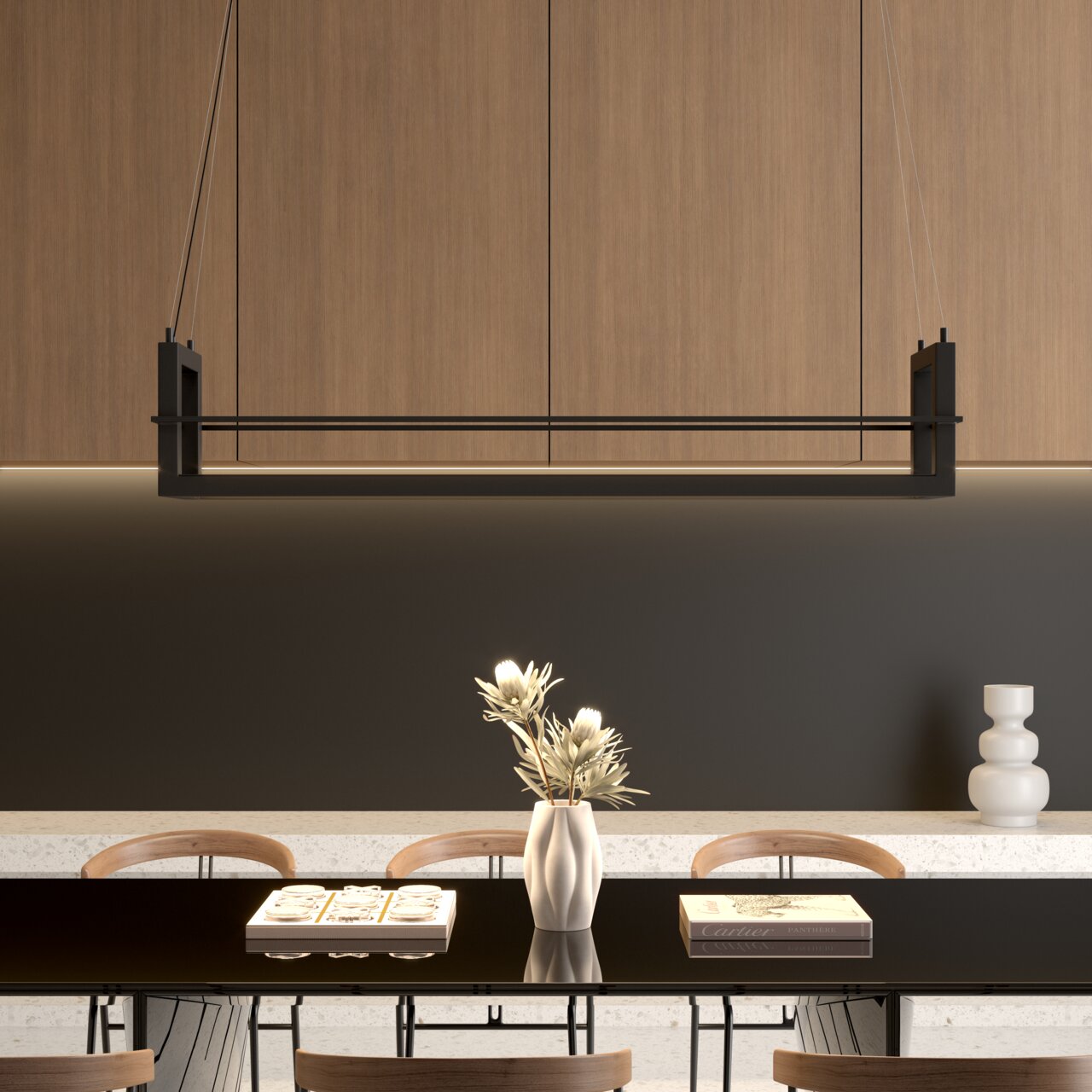 Moderne, rechthoekige hanglamp in zwart boven een eettafel, gezien van voren; op de achtergrond houten kasten en een donkere muur, op de tafel een vaas en boeken.