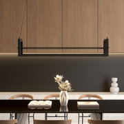 Moderne, rechthoekige hanglamp in zwart boven een eettafel, gezien van voren; op de achtergrond houten kasten en een donkere muur, op de tafel een vaas en boeken.