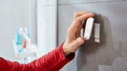 Hand befestigt einen tesa Powerstrip Waterproof Haken an einer Badezimmerwand, seitliche Perspektive.