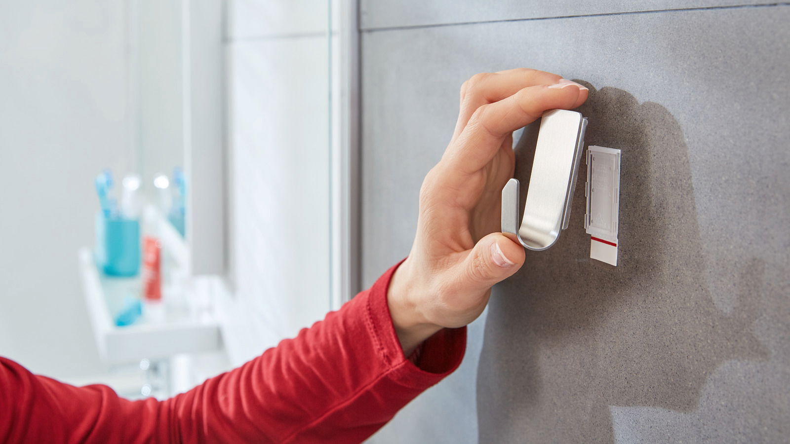Hand befestigt einen tesa Powerstrip Waterproof Haken an einer Badezimmerwand, seitliche Perspektive.
