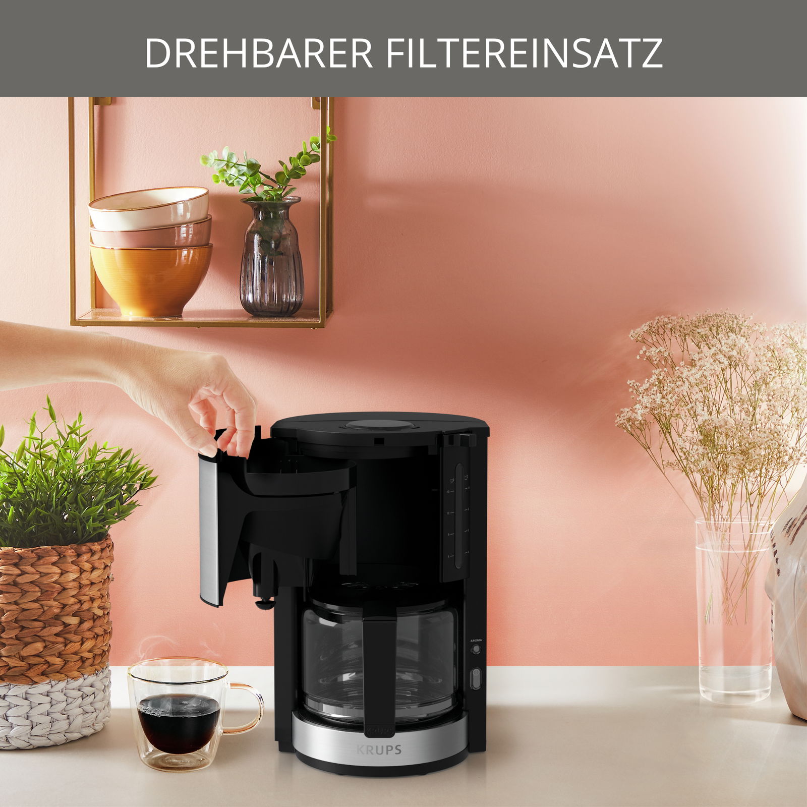 Kaffeemaschine ProAroma Plus mit drehbarem Filtereinsatz, seitliche Perspektive, in einer modernen Küche mit Pflanzen und Geschirr im Hintergrund.