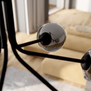 Detailfoto vanuit zijaanzicht: glanzende verchroomde bol op een zwart metalen frame, waarschijnlijk onderdeel van een moderne lamp, tegen een onscherpe houten vloer en een raam