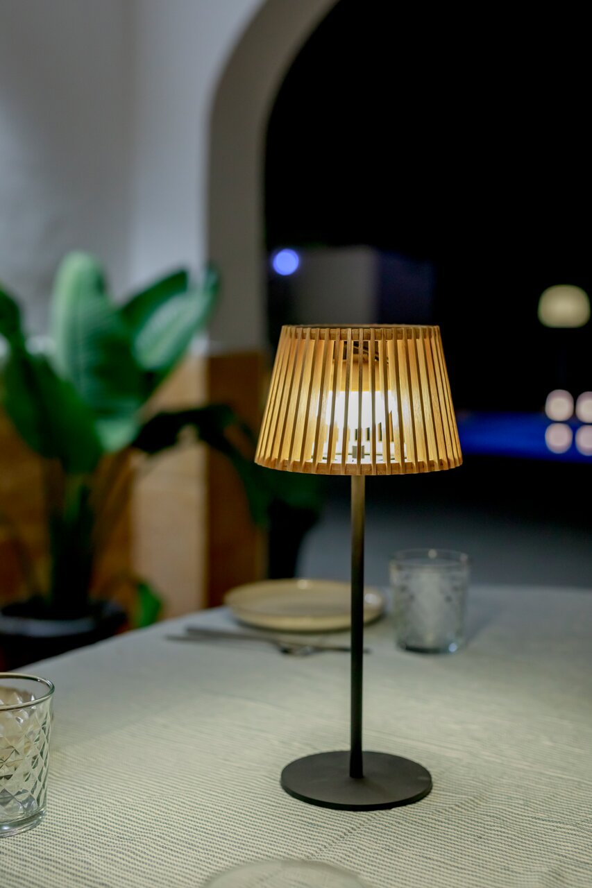 Solar-Tischleuchte mit Holzlamellen, auf einem Tisch bei Nacht, seitliche Perspektive