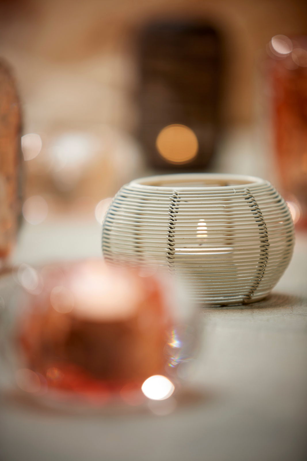 Nahaufnahme eines runden, weißen Teelichthalters mit Rattan-Optik, umgeben von unscharfen Lichtern im Hintergrund.