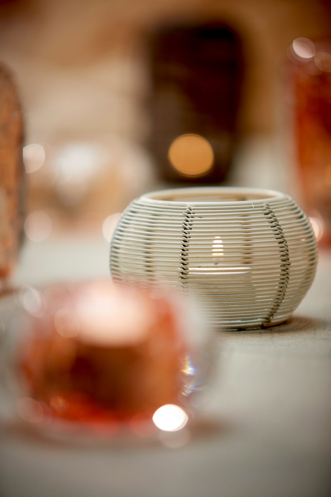 Nahaufnahme eines runden, weißen Teelichthalters mit Rattan-Optik, umgeben von unscharfen Lichtern im Hintergrund.