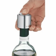 Nahaufnahme eines Weinflaschenverschlusses aus Metall, der auf eine geöffnete Weinflasche gesetzt wird. Eine Hand drückt den Verschluss von oben herunter.
