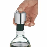 Nahaufnahme eines Weinflaschenverschlusses aus Metall, der auf eine geöffnete Weinflasche gesetzt wird. Eine Hand drückt den Verschluss von oben herunter.