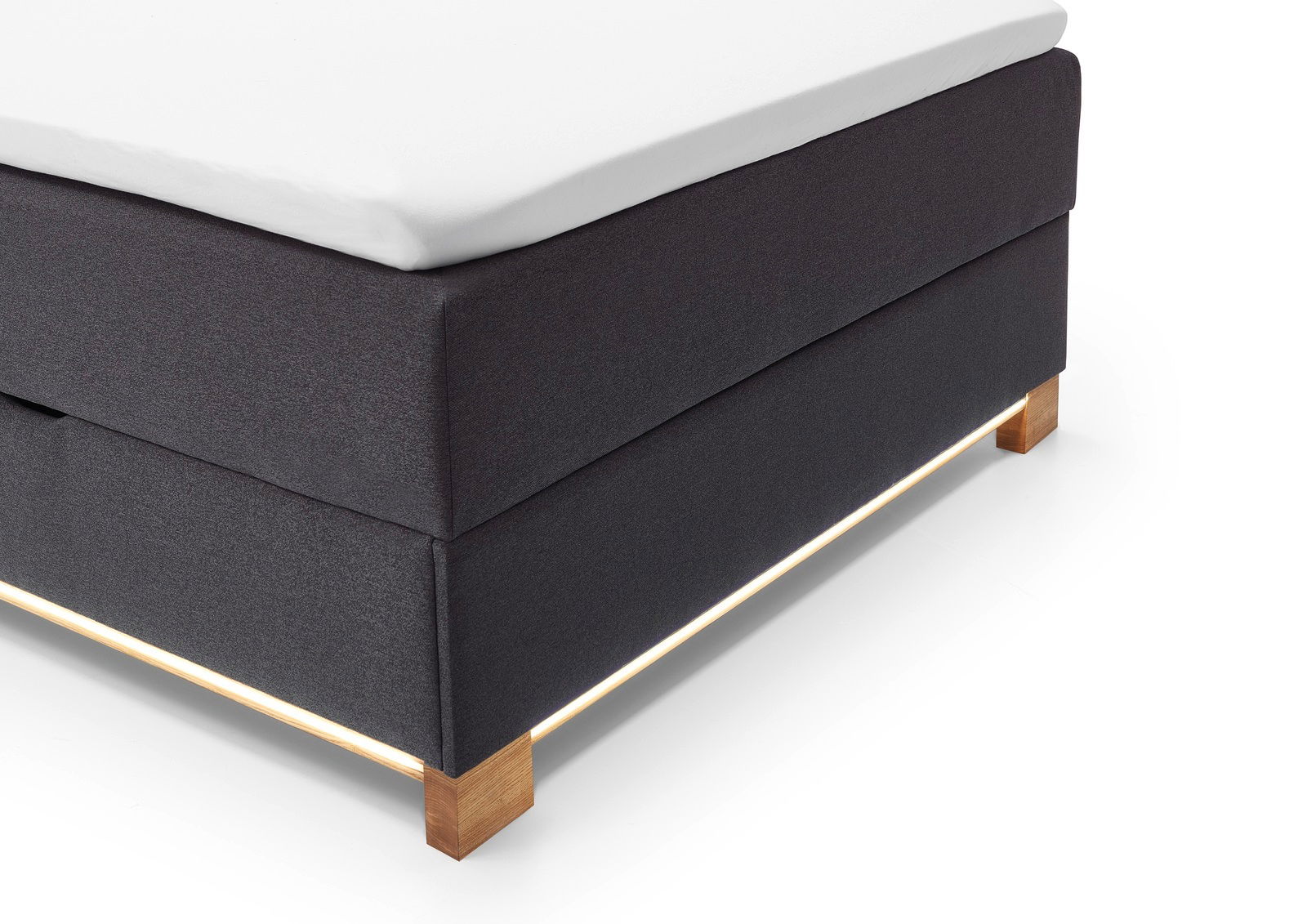 Ecke eines Boxspringbetts mit dunklem Stoffbezug und Holzfüßen, seitliche Perspektive