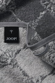 Nahaufnahme eines grauen Gästetuchs mit geometrischem Muster und einem schwarzen Etikett mit der Aufschrift 'JOOP!'