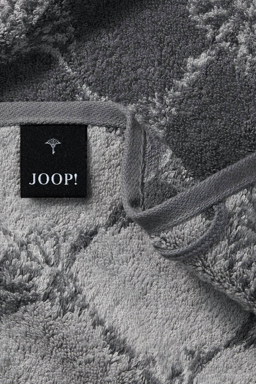 Nahaufnahme eines grauen Gästetuchs mit geometrischem Muster und einem schwarzen Etikett mit der Aufschrift 'JOOP!'