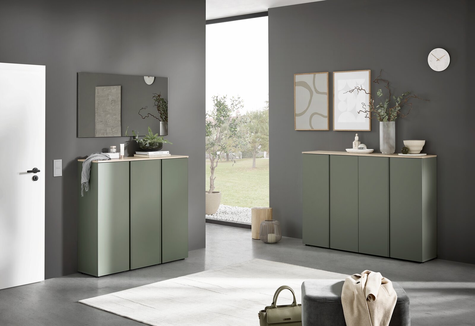 Modernes Sideboard in mattem Salbeigrün mit heller Holzplatte in einem minimalistischen Wohnraum, frontale Perspektive mit leichtem Blick von links; dekoriert mit Pflanzen, Bildern und Spiegel an grauer Wand.