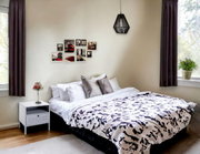 Modernes Schlafzimmer mit Doppelbett, weißer Bettwäsche mit schwarz-grauem Muster, grauen Kissen, Nachttisch und Hängelampe; Frontansicht leicht schräg von links.