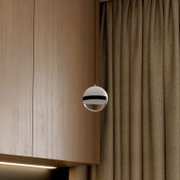 Moderne kugelförmige Pendelleuchte in Weiß mit schwarzem Ring und verspiegelter Unterseite vor Holzpaneel und braunem Vorhang, seitliche Nahaufnahme aus leicht unterer Perspektive