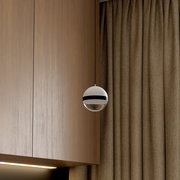 Moderne kugelförmige Pendelleuchte in Weiß mit schwarzem Ring und verspiegelter Unterseite vor Holzpaneel und braunem Vorhang, seitliche Nahaufnahme aus leicht unterer Perspektive
