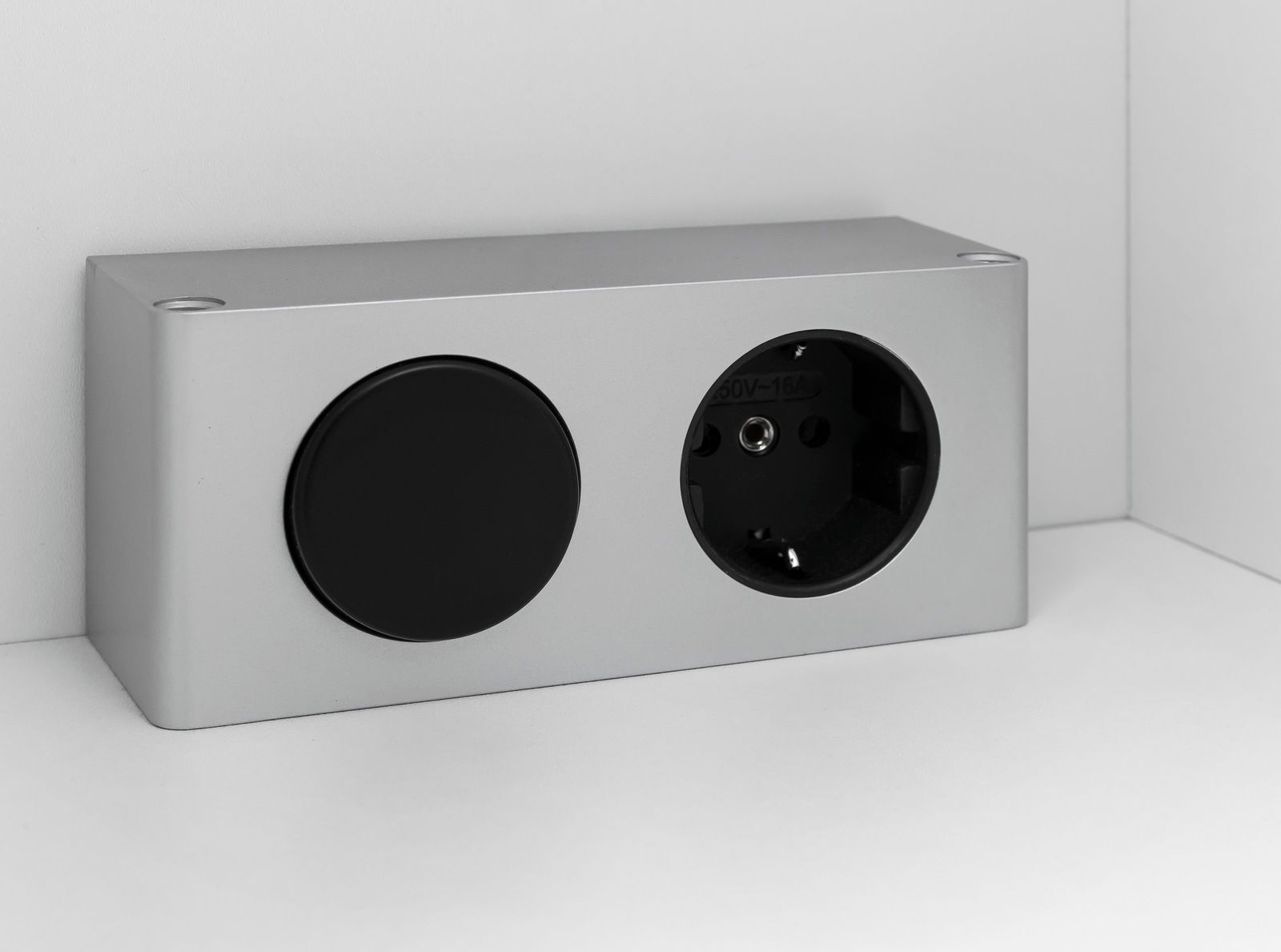 Silberne Steckdose mit zwei Anschlüssen, eine runde Abdeckung und eine Steckdose, seitliche Perspektive.