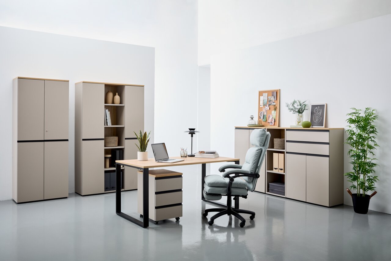 Moderne Büromöbel in einem hellen Raum, bestehend aus einem Schreibtisch mit Rollcontainer, einem ergonomischen Bürostuhl und mehreren Aktenschränken. Perspektive von vorne.