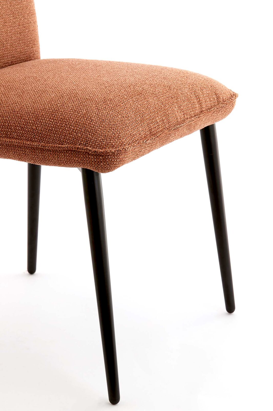 Detailfoto van een gestoffeerde stoel met een terracottakleurige stoffen bekleding en zwarte metalen poten, schuin van rechtsvoor gefotografeerd, met de camera gericht op de zitting en de poten