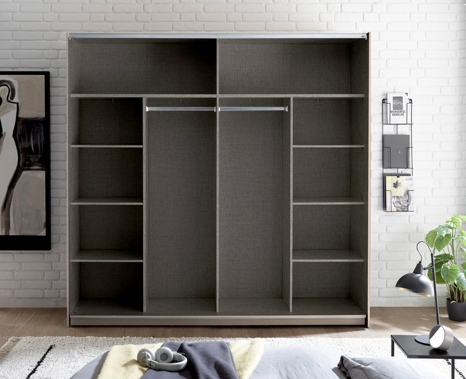 Offener Kleiderschrank in grauer Holzoptik mit Regalfächern links und rechts sowie zwei mittigen Kleiderstangen, frontal von vorn in einem hellen Schlafzimmer fotografiert.
