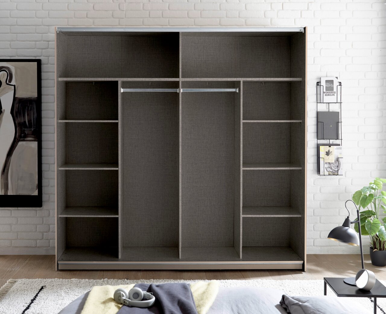 Offener Kleiderschrank in grauer Holzoptik mit Regalfächern links und rechts sowie zwei mittigen Kleiderstangen, frontal von vorn in einem hellen Schlafzimmer fotografiert.