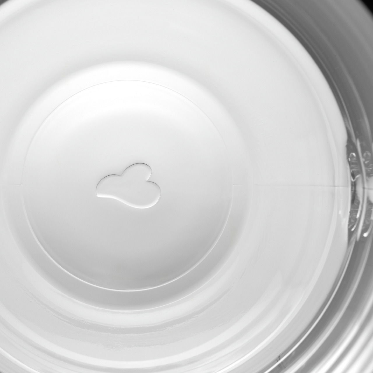 Blick von oben in eine weiße Tasse mit einem herzförmigen Relief am Boden.