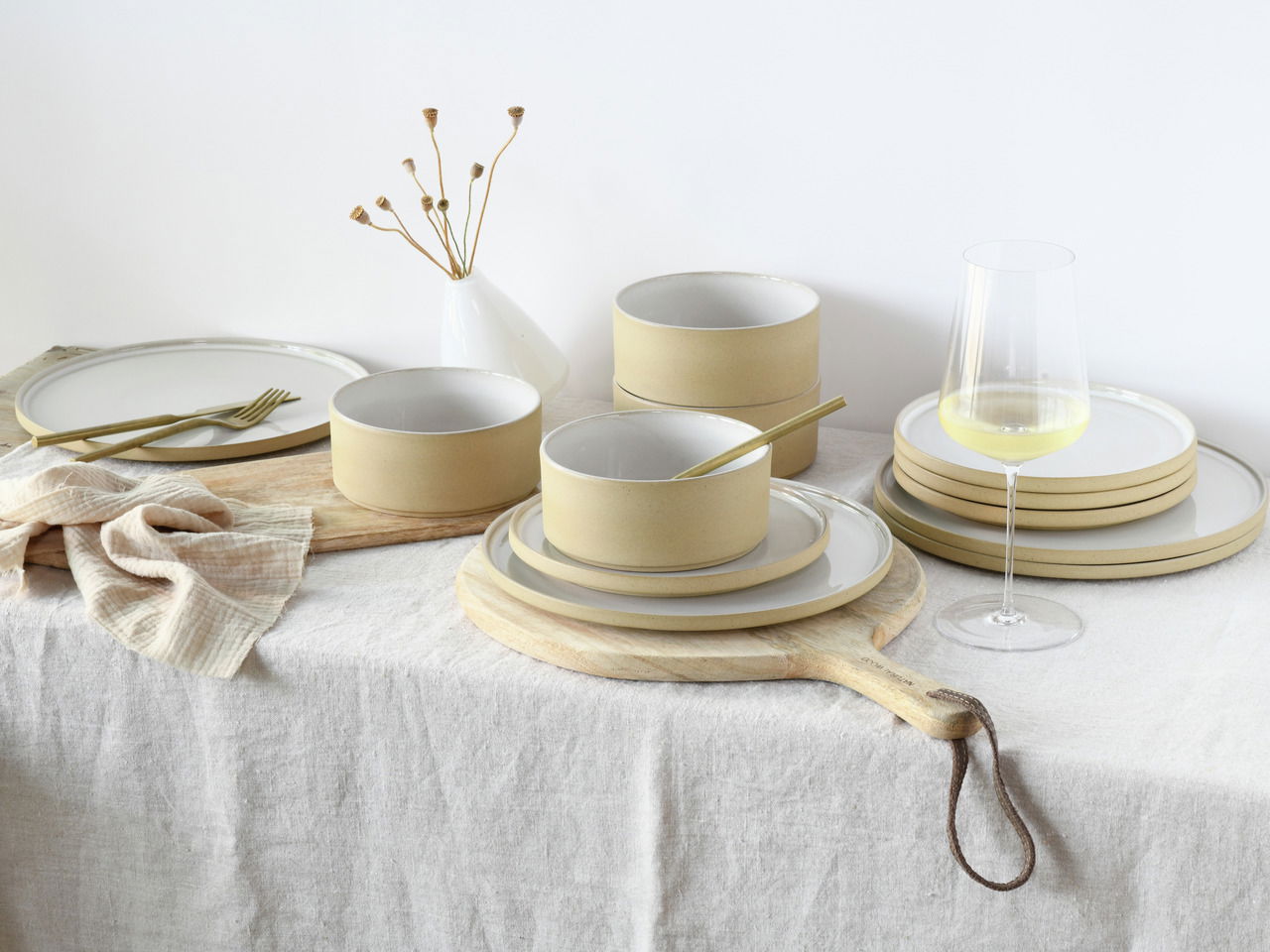 Tellerset Futuro White Sand 12, bestehend aus eleganten, sandfarbenen Tellern und Schalen, arrangiert auf einem Tisch mit natürlichem Leinenstoff, aus seitlicher Perspektive fotografiert.