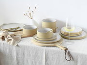 Tellerset Futuro White Sand 12, bestehend aus eleganten, sandfarbenen Tellern und Schalen, arrangiert auf einem Tisch mit natürlichem Leinenstoff, aus seitlicher Perspektive fotografiert.