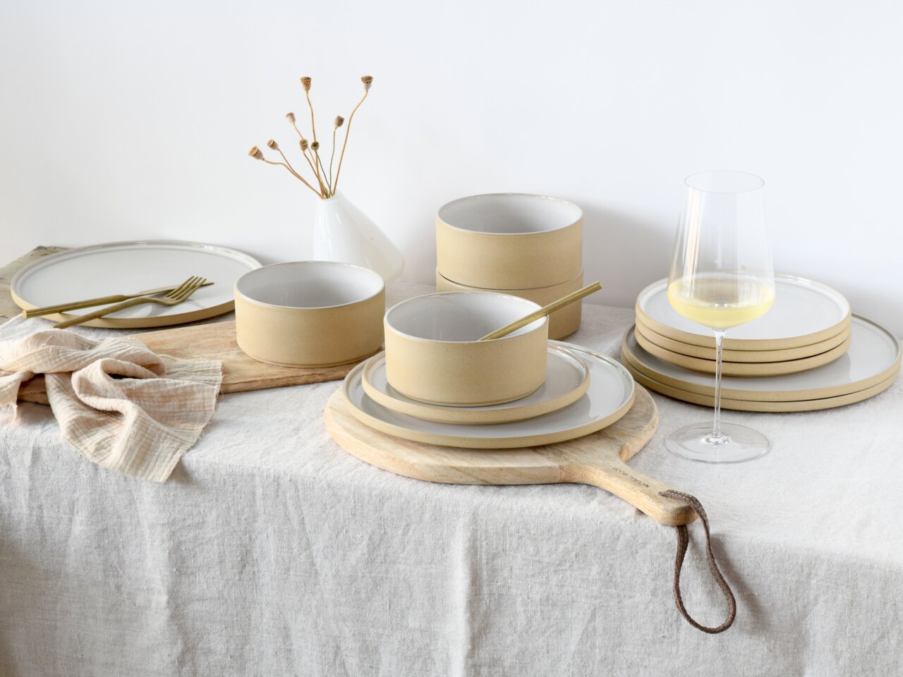 Tellerset Futuro White Sand 12, bestehend aus eleganten, sandfarbenen Tellern und Schalen, arrangiert auf einem Tisch mit natürlichem Leinenstoff, aus seitlicher Perspektive fotografiert.