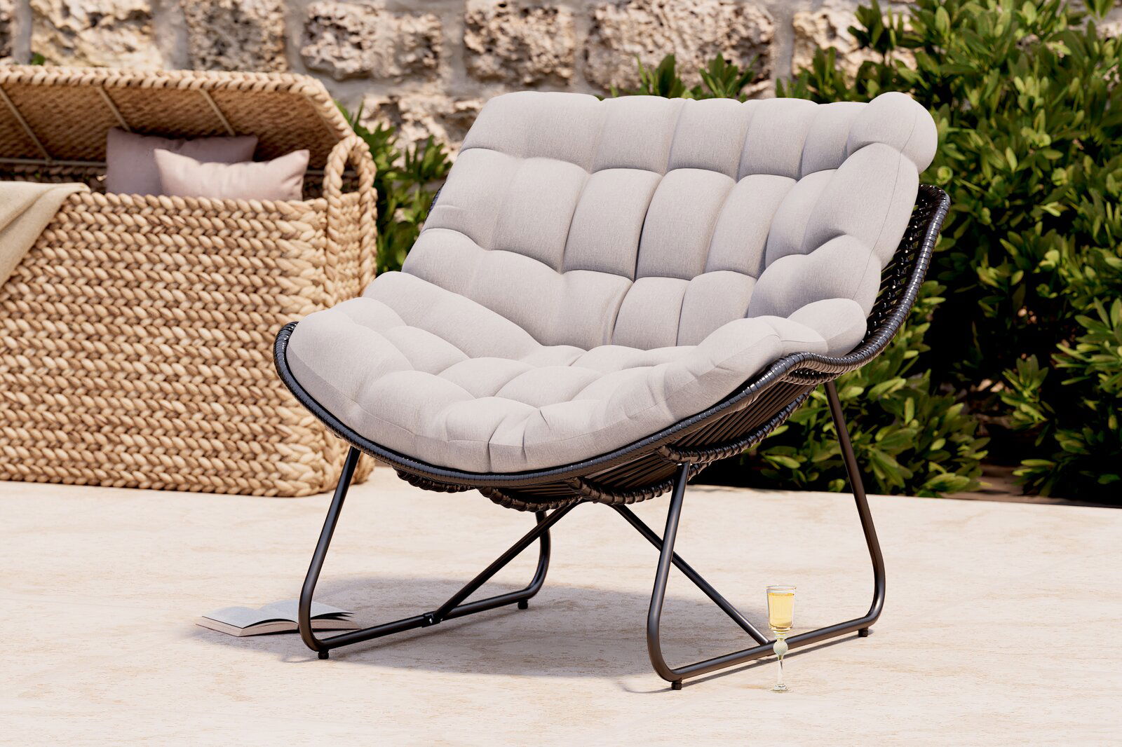 Bequemer Relaxsessel mit gepolstertem, hellgrauem Kissen und schwarzem Metallrahmen, seitliche Perspektive, im Freien aufgestellt.