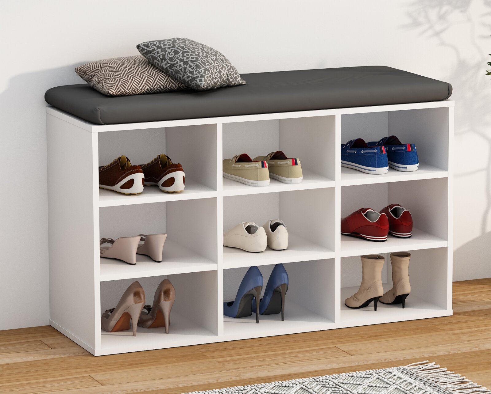 Weißes Schuhregal mit 9 offenen Fächern und schwarzem Sitzkissen, mit Schuhen bestückt und zwei Kissen obenauf, Ansicht schräg von vorne links.