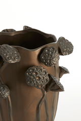 Nahaufnahme einer bronzefarbenen Vase mit erhabenen, blütenartigen Verzierungen. Die Perspektive zeigt die obere Hälfte der Vase.