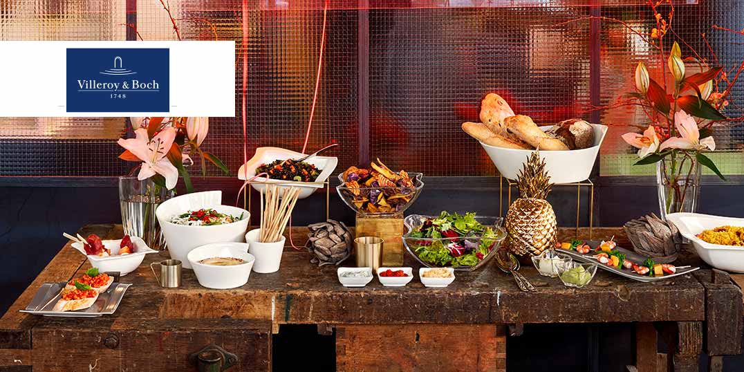 Ein festlich gedeckter Holztisch mit Brot, Salaten, Obst und exotischer Dekoration in warmem Licht.