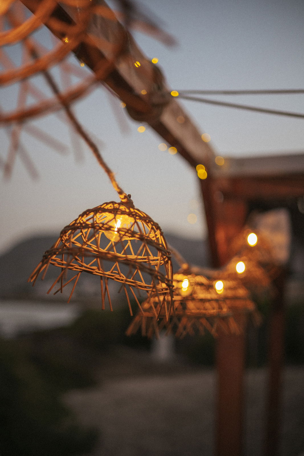 Nahaufnahme einer Outdoor-Solarlichterkette mit dekorativen Lampenschirmen aus Rattan, aufgehängt an einem Holzrahmen in der Abenddämmerung.