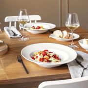 Ein stilvoll gedeckter Tisch mit zwei Weißweingläsern, gefüllt mit Weißwein, und eleganten weißen Tellern, die mit frischen Speisen angerichtet sind. Die Perspektive zeigt eine einladende Tischszene von schräg oben.