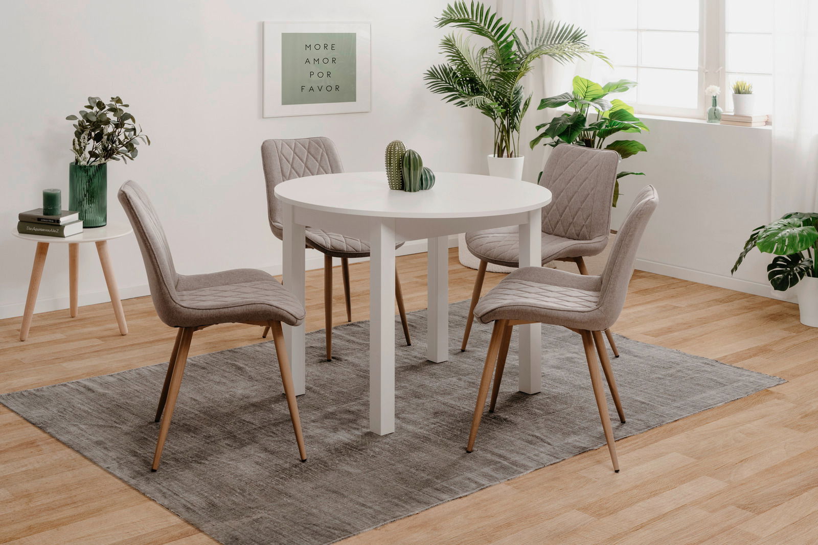 Runder weißer Esstisch mit vier grauen Stühlen in einem modernen, hellen Raum mit Pflanzen, aus seitlicher Perspektive.