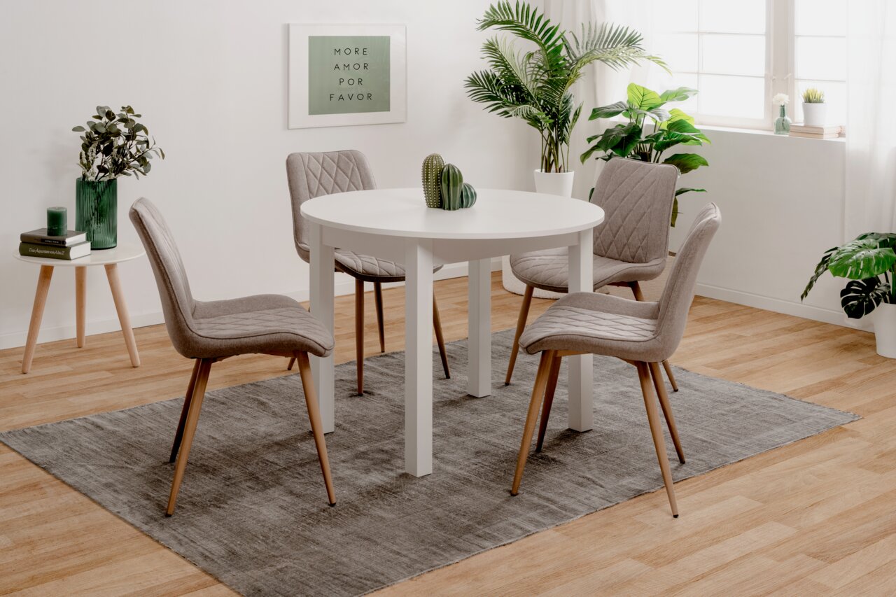 Z2 Ronde functionele eettafel COBURG Ronde witte eettafel met vier grijze stoelen in een moderne, lichte ruimte met planten, gezien vanuit een zijdelingse hoek.