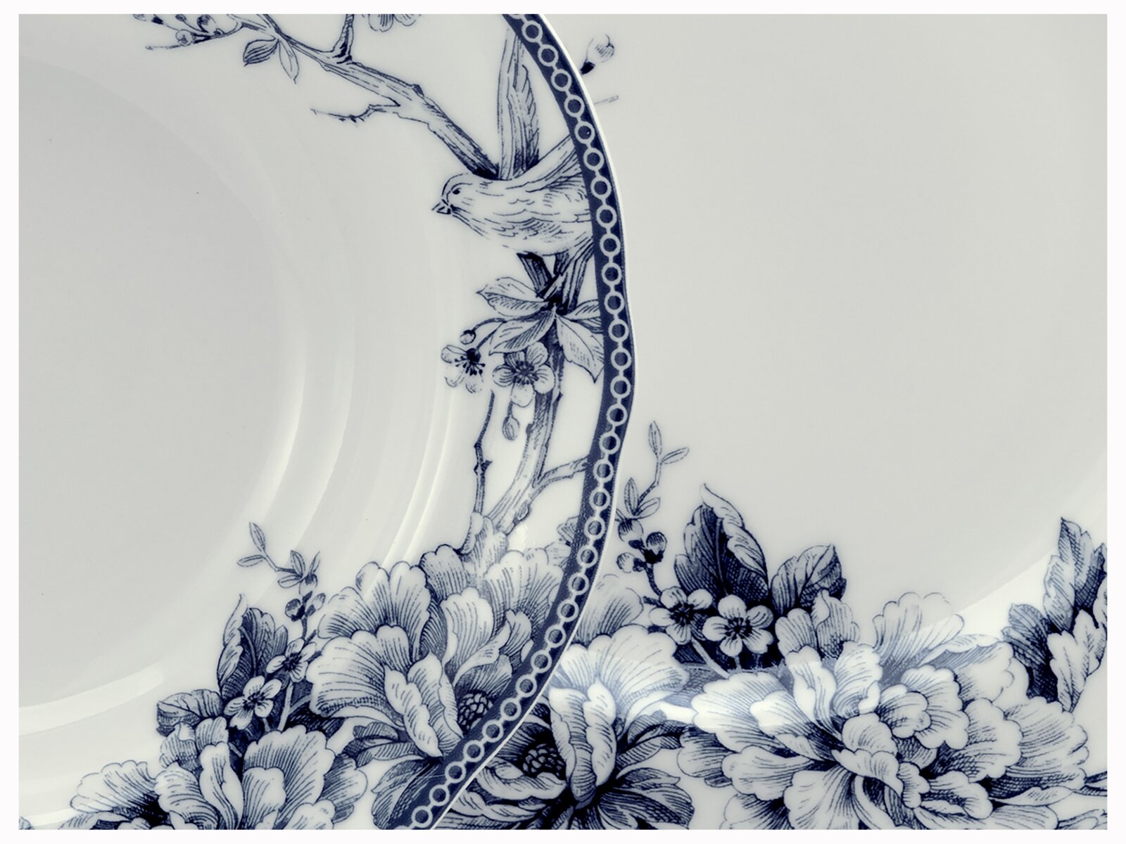 Detailaufnahme aus schräger Draufsicht: weißer Porzellanteller mit blauem Blumen- und Vogel-Dekor sowie gepunktetem Rand