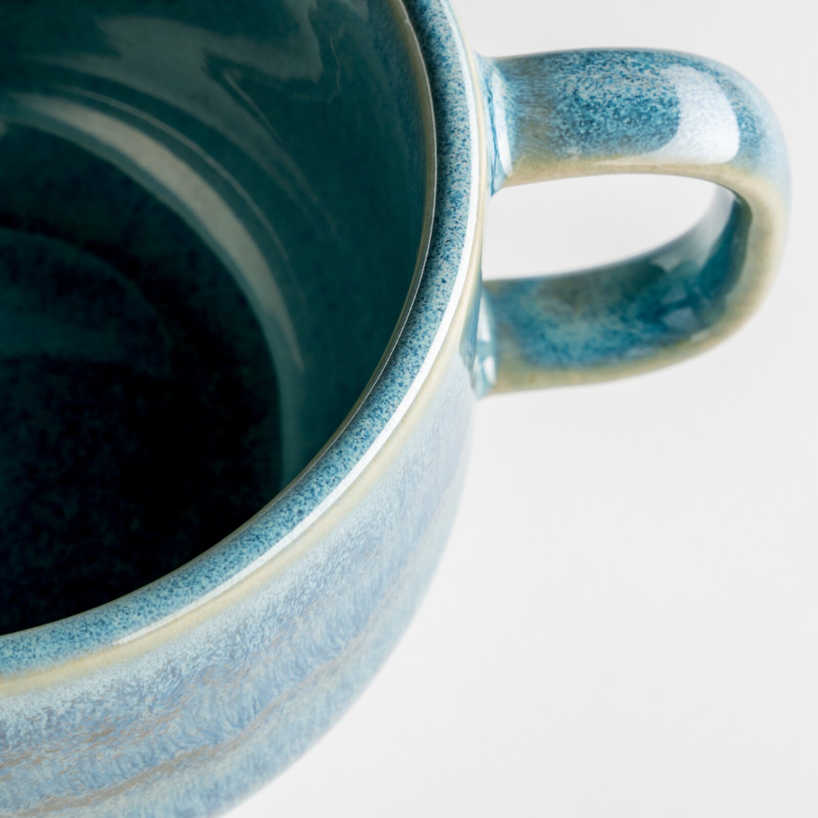 Detailaufnahme einer blau glasierten Keramik-Tasse mit Henkel, schräg von oben/seitlich vor weißem Hintergrund